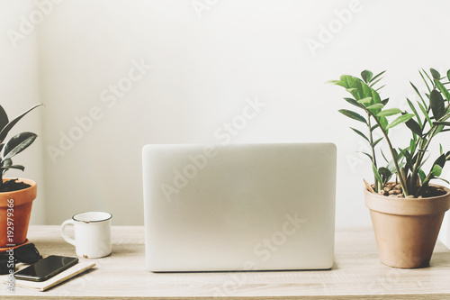 Laptop on wooden desktop with phone  notebook  coffee cup and plant in stylish modern room. Freelance concept. business workspace in home or office. stylish work place. working online