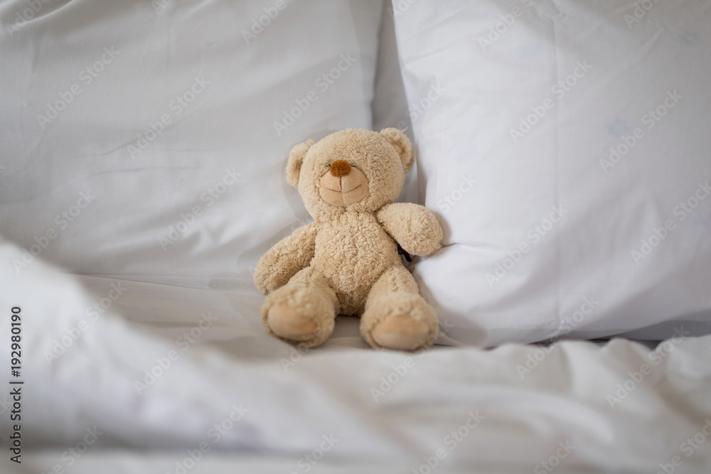 Sleeping teddy bear on white bed.