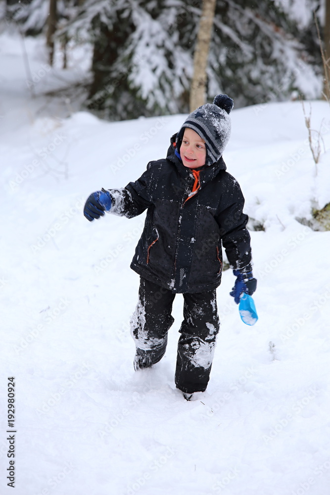 Little boy running up the snowy hill with blue shovel