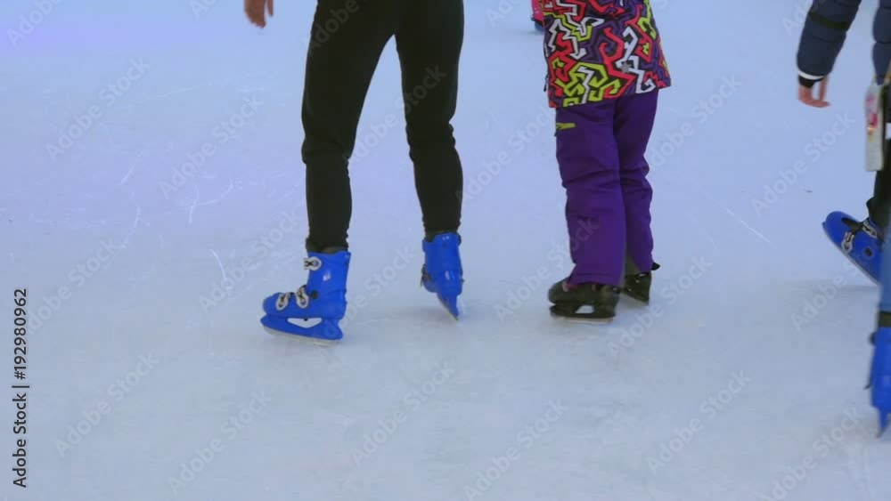 Closeup on kids learning ice skating on artificial ice rink. Closeup on skates on feets moving round in circles. Closeup on kids learning ice skating on artificial ice rink. Closeup on skates on feets moving round in circles.