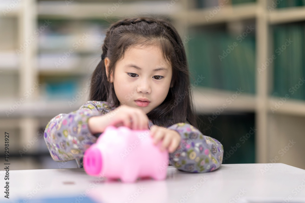Kids playing collect money with a pink saving Pig Jar in the Library. Setup studio shooting. Kids playing collect money with a pink saving Pig Jar in the Library. Setup studio shooting.