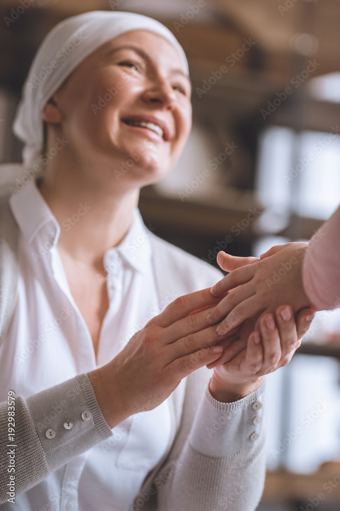 Obraz premium cropped shot of child and smiling sick mature woman in kerchief holding hands