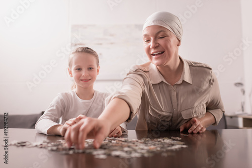 smiling kid with sick grandmother in kerchief playing with jigsaw puzzle together