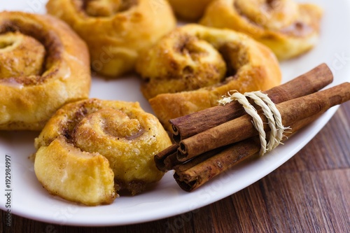 Homemade cinnamon rolls with sugar glazing on white oval plate and a bunch of cinnamon sticks
