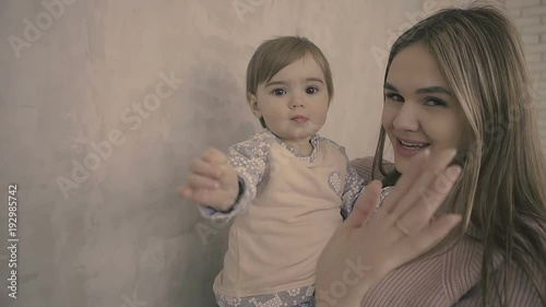 Brunette Mother and daughter stay in Studio. Mom holds her daughter in her arms near gray wall. There is a free place for text. slow motion