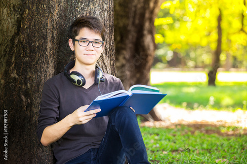 Photography student read a book and listen music by earphone with happy and relax in park