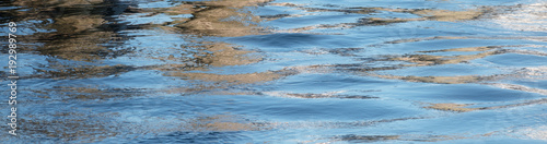 Blue water surface with small ripples or waves and dark reflections as a panoramic banner background with copy space