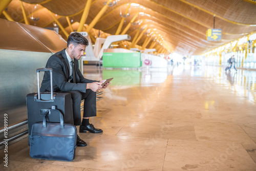 young businessman with tablet smiling at the airport and waiting for his flight with luggage