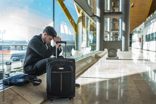 young businessman upset at the airport waiting his delayed flight with luggage