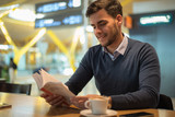 young man at the airport reading a book and drinking coffee waiting for his flight
