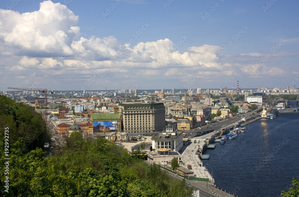 Kiev, the capital of Ukraine areal view with cloudy sky over river Dnieper, old historical district Podil with river port and modern buildings at the left bank of the river on the background.
