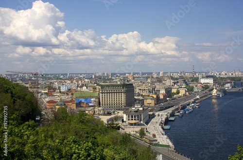 Kiev, the capital of Ukraine areal view with cloudy sky over river Dnieper, old historical district Podil with river port and modern buildings at the left bank of the river on the background. © Maryna