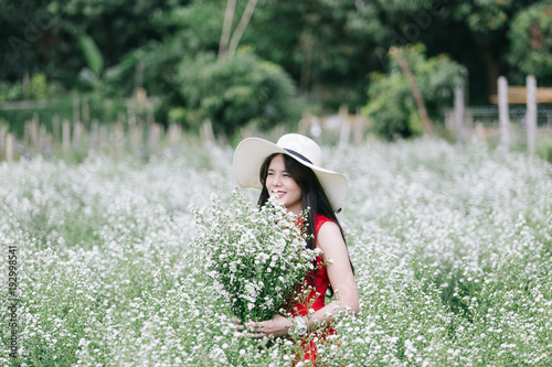 Portrait young woman in red dress smelling white cutter flower in garden. © Somkiat