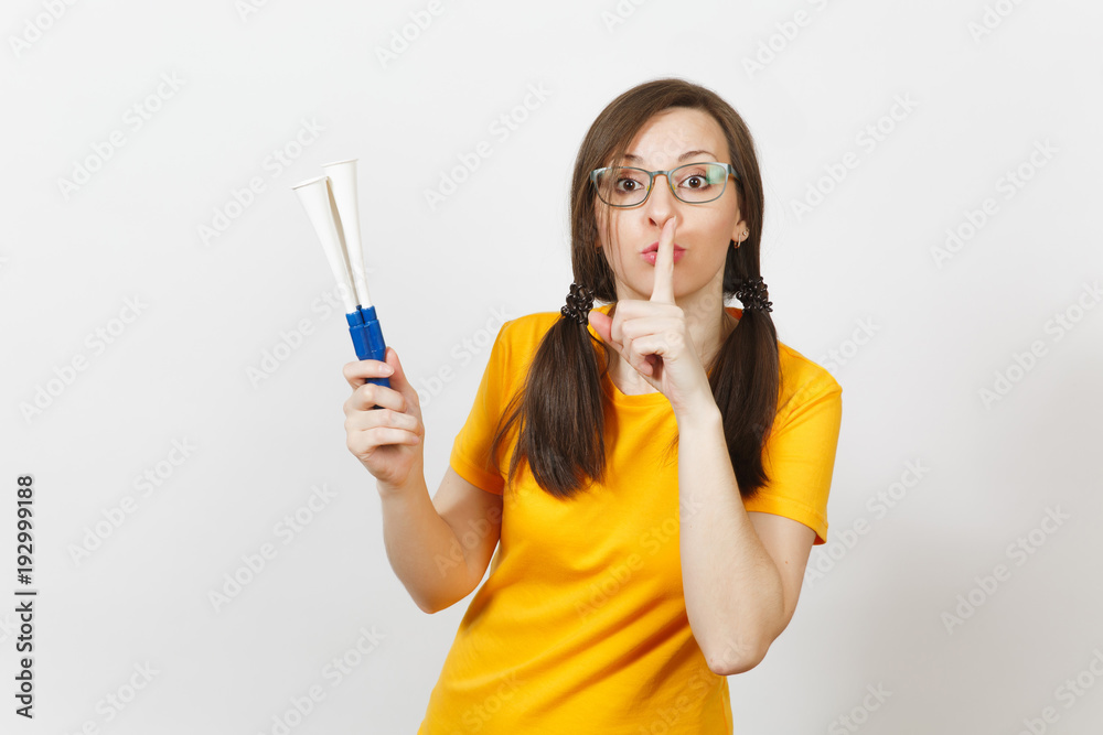 European young woman fun pony tails fan or player in glasses yellow uniform say hush be quiet with finger on lips gesture, hold football pipe isolated on white background. Sport fan lifestyle concept. European young woman fun pony tails fan or player in glasses yellow uniform say hush be quiet with finger on lips gesture, hold football pipe isolated on white background. Sport fan lifestyle concept.