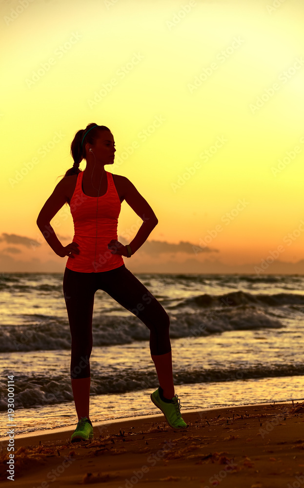 Silhouette of young woman in sportswear standing on seacoast