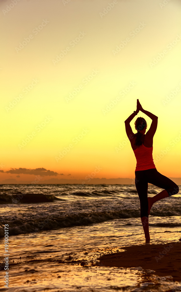 Silhouette of fit woman in sport clothes on seacoast doing yoga