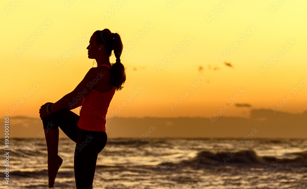 active woman in sport clothes on seashore stretching. Silhouette
