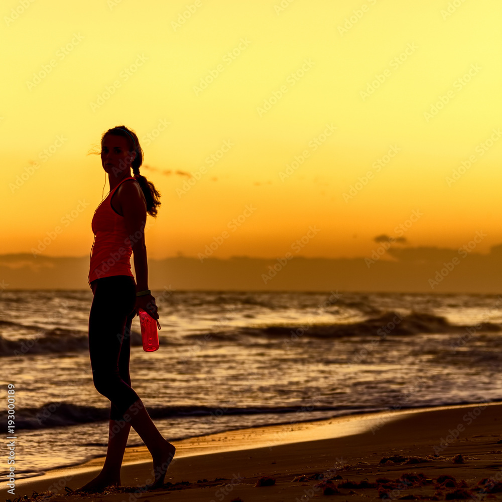 healthy woman in sportswear on beach with bottle of water