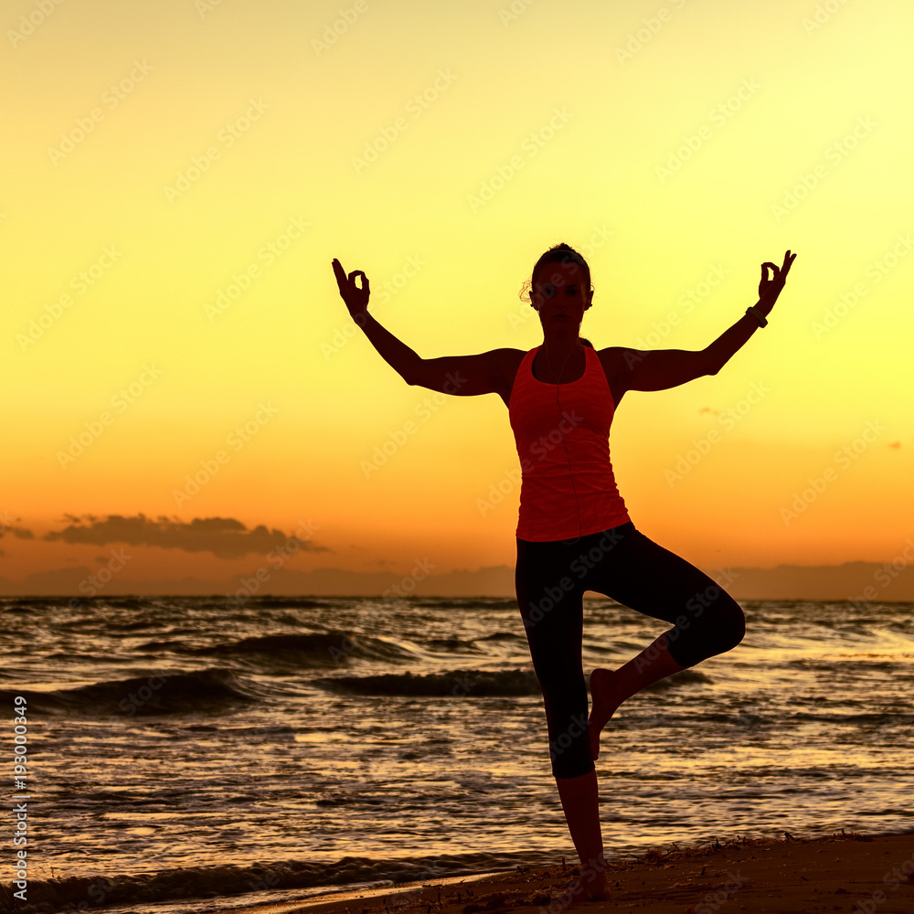 Silhouette of healthy woman in sportswear on seashore doing yoga