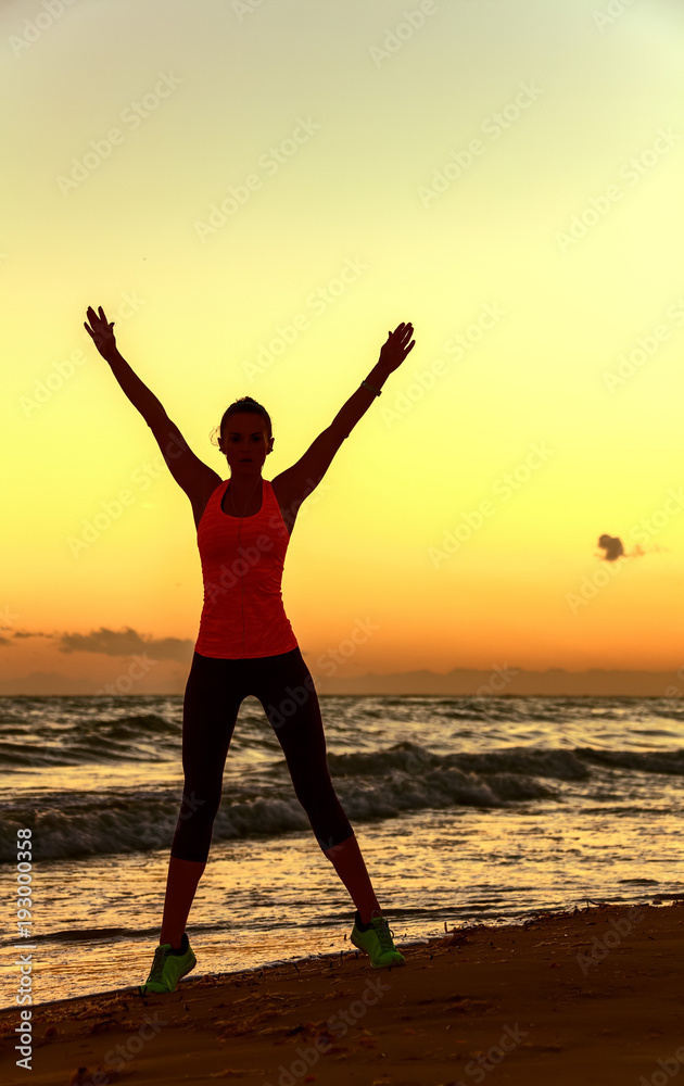 Silhouette of fit woman in sports gear on beach rejoicing