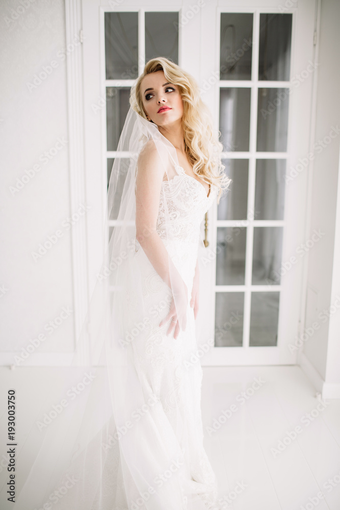 Wedding. Bride in a beautiful dress indoors in a white studio, like at home. The fashionable wedding style is taken in full length. Young attractive blond model with curly hair, like a bride Wedding. Bride in a beautiful dress indoors in a white studio, like at home. The fashionable wedding style is taken in full length. Young attractive blond model with curly hair, like a bride