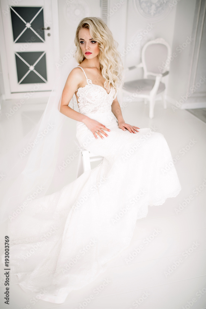 Wedding. Bride in a beautiful dress indoors in a white studio, like at home. The fashionable wedding style is taken in full length. Young attractive blond model with curly hair, like a bride Wedding. Bride in a beautiful dress indoors in a white studio, like at home. The fashionable wedding style is taken in full length. Young attractive blond model with curly hair, like a bride