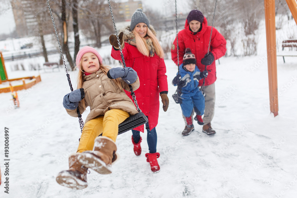 Picture of girl and boy swinging in winter in park with parents