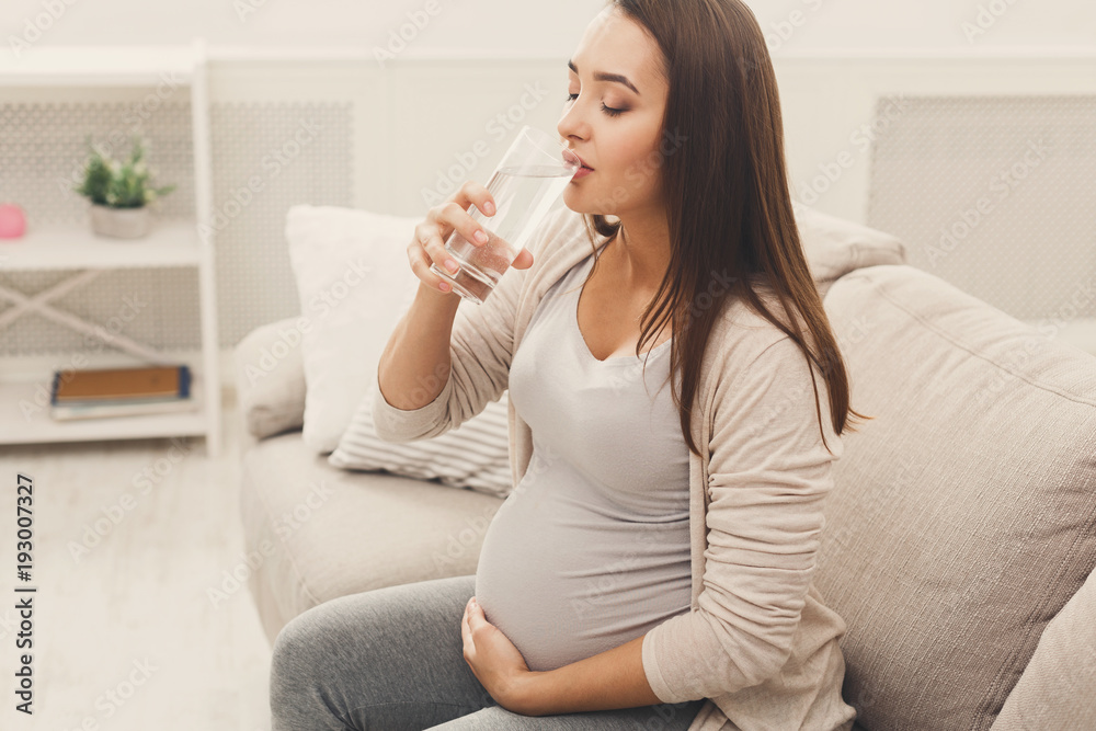 Pregnant woman drinking water sitting on sofa Pregnant woman drinking water sitting on sofa