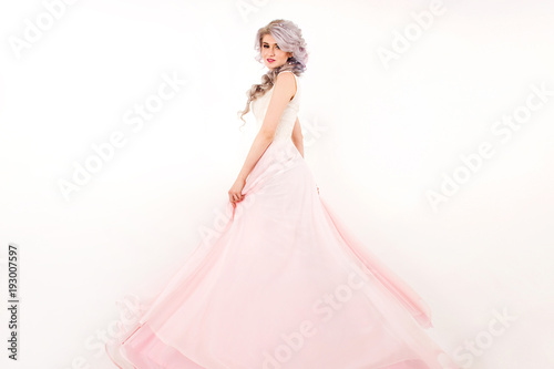 a young girl in a white pink dress is standing and smiling on a white wall background