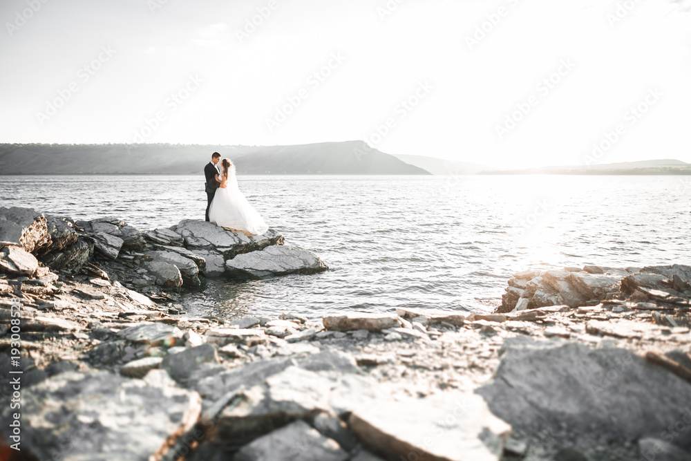 Wedding couple kissing and hugging on rocks near blue sea Wedding couple kissing and hugging on rocks near blue sea