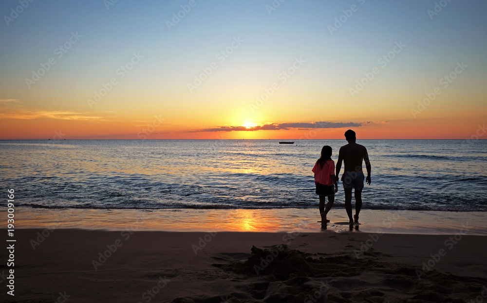 A man and his daughter walking on the beach during sunset