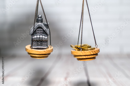 Stack of coins and a small house on the scales. The concept of choice, cash savings and purchase of real estate.