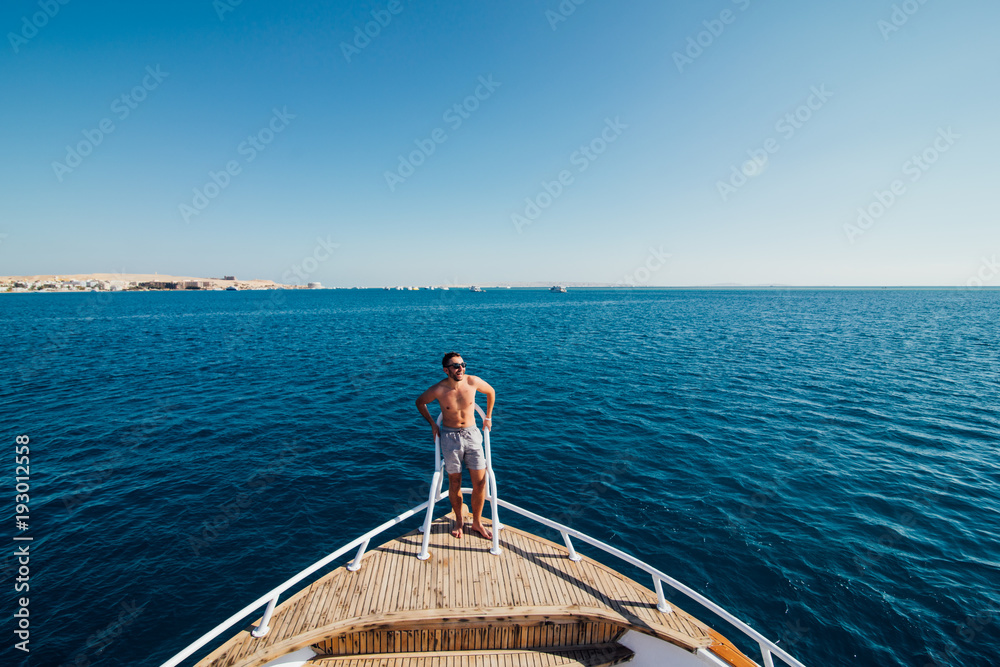 Handsome man standing on the deck of yacht and resting under the sun in the sea