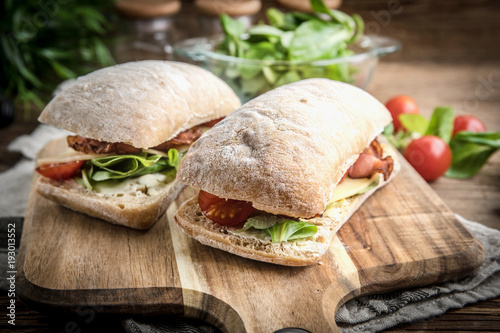 Photos Ciabatta sandwich with arugula salad, bacon and yellow cheese.