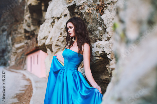 Sexy brunette stands next to a mountain in a blue dress