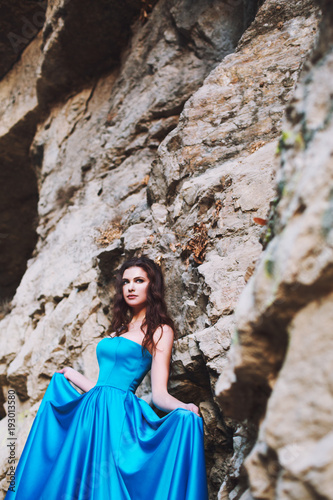 A sweet girl is standing next to a mountain in a blue dress