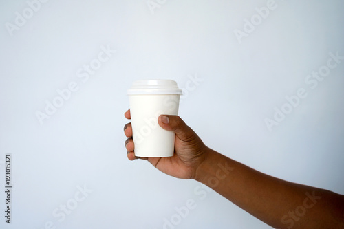 The hand of a dark-skinned man holds a disposable cup for coffee or tea background a white and blue wall. Side view with copy space