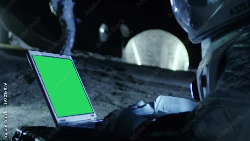 Astronaut on the Alien Planet Works on a Mock-up Green Screen Laptop. In the Background Her Crew Member and Space Habitat. Extraterrestrial Colonization Concept. 