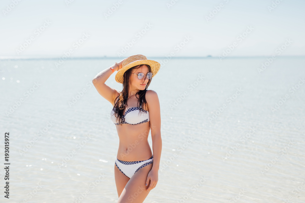 Young sexy slim girl standing on a beach wearing white bikini swimwear on sea background