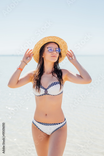 Happy woman on the beach in sunglasses and a straw hat on blue sea water