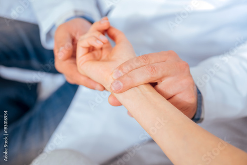 Taking care of your health. Close up of medical worker putting his fingers on a wrist of a female patient while checking her pulse during an appointment.