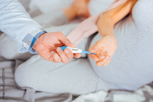 Taking care of a baby. Scaled up look on hands of a pregnant woman and a doctor holding thermometer during an appointment.