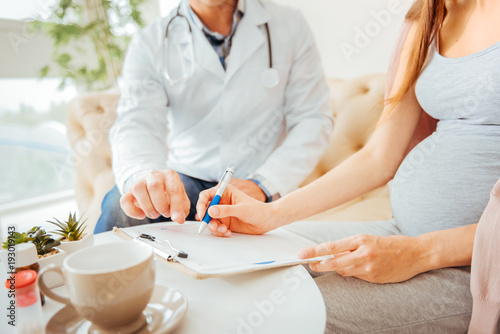 Personal data. Scaled up look on an expectant mother writing next to a doctor and writing something down in a clinic.