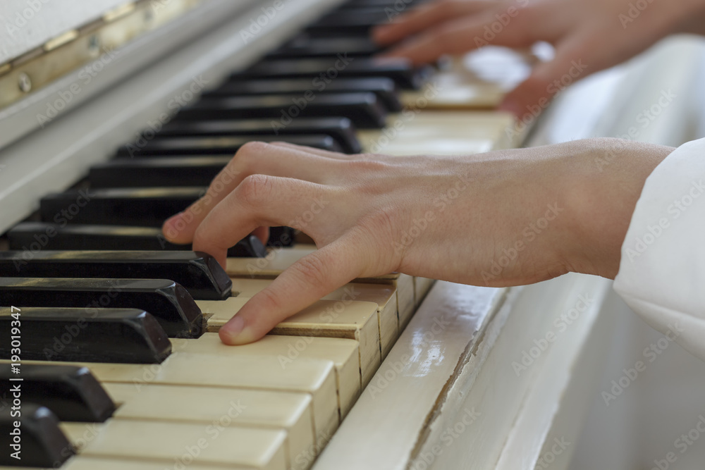 Fototapeta premium Hands of a young girl playing on a white piano, close-up.