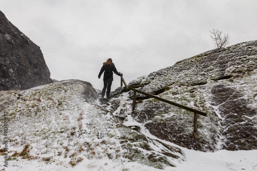 Woman walking alone, climbing a mountain in snowy weather.