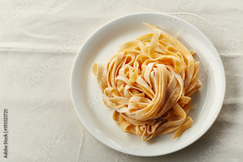 Handmade italian tagliatelle pasta on white plate uncooked
