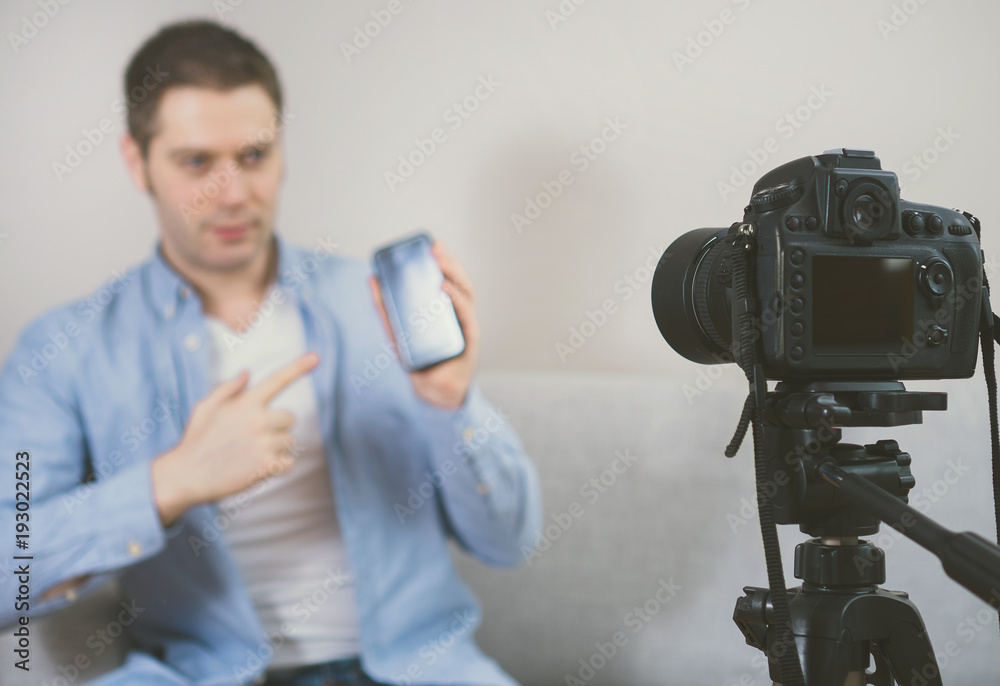 Man making video blog about mobile phones. Focus on camera.