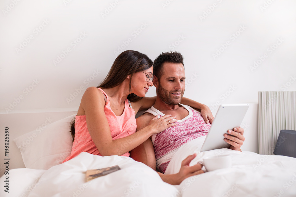 Couple using digital tablet while sitting on bed Couple using digital tablet while sitting on bed