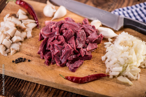 chopped sliced raw uncooked meat with garlick peppercorns chillies on wood background