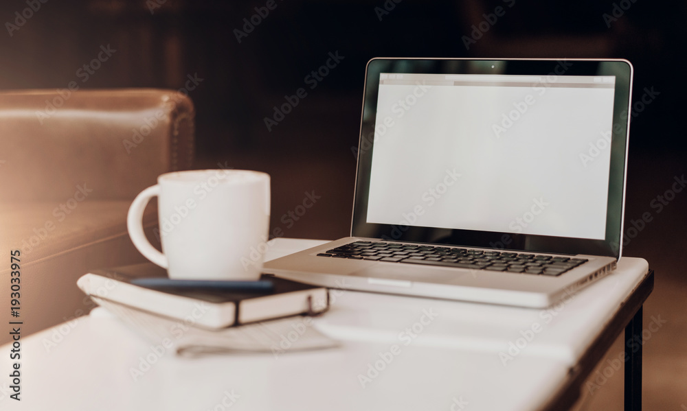 Front view. Empty workplace. On white coffee table is laptop with blank screen, cup of coffee, notebook, pen, newspaper. Place for logo, text, template. Mock up. Telework, distance work online Front view. Empty workplace. On white coffee table is laptop with blank screen, cup of coffee, notebook, pen, newspaper. Place for logo, text, template. Mock up. Telework, distance work online